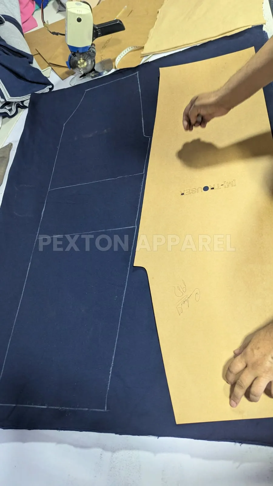 Marking a paper pattern on navy fabric before cutting at Pexton Apparel